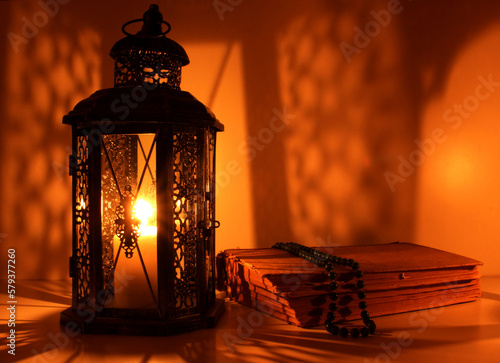 Ornamental Arabic lantern with burning candle glowing at night and glittering golden bokeh lights. Festive greeting card, an invitation for the Muslim holy month Ramadan Kareem. Dark background.