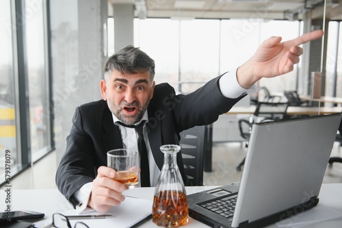 Old business man is drinking alchool at the office photo