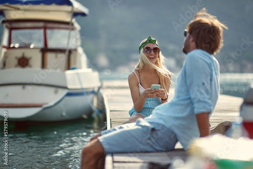young couple sitting on a dock, talking, smiling, laughing, enjoying at the seaside