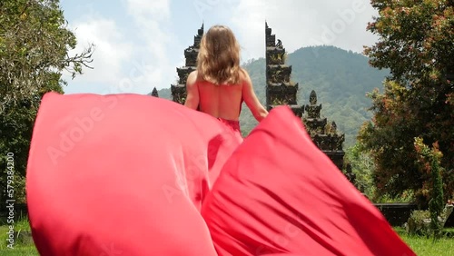 Pretty asian woman walks to balinese gates in long red dress in slowmotion on Hangara gates in Bali Indonesia. High quality fullhd footage