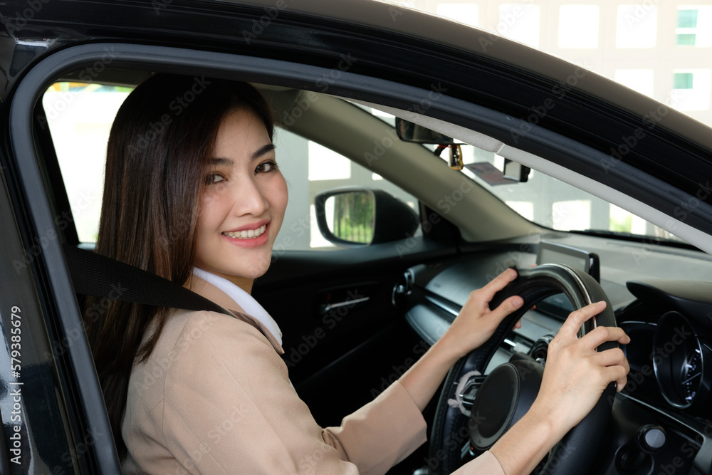 Beautiful happy successful businesswoman is driving a new modern car in good mood. Portrait cute female driver steering car with safety belt.