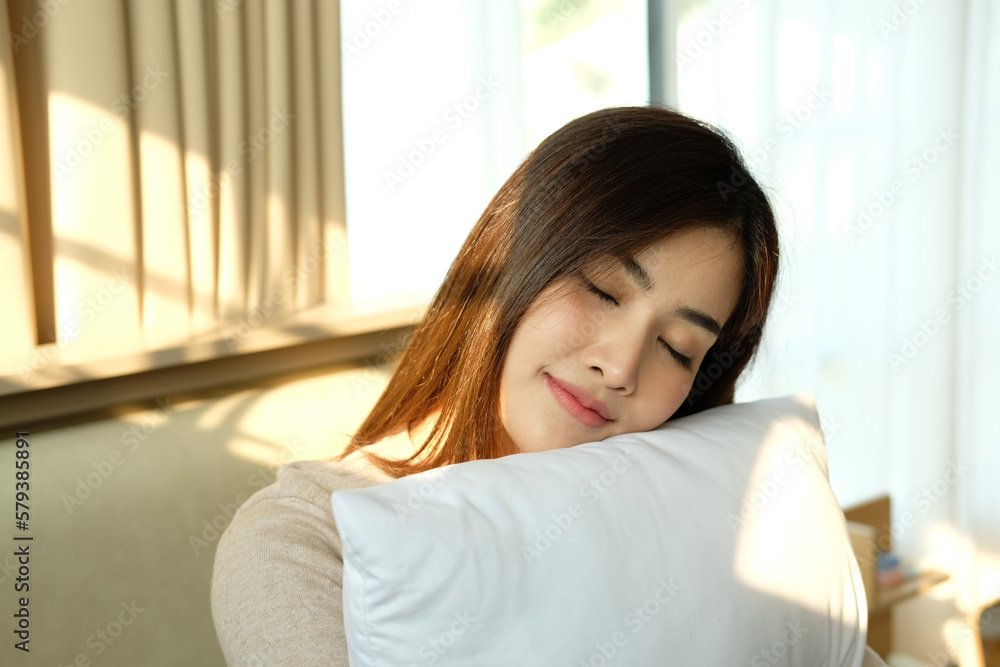 Young woman hugging pillow on comfortable bed with silky linens Young woman hugging pillow on comfortable bed with silky linens
