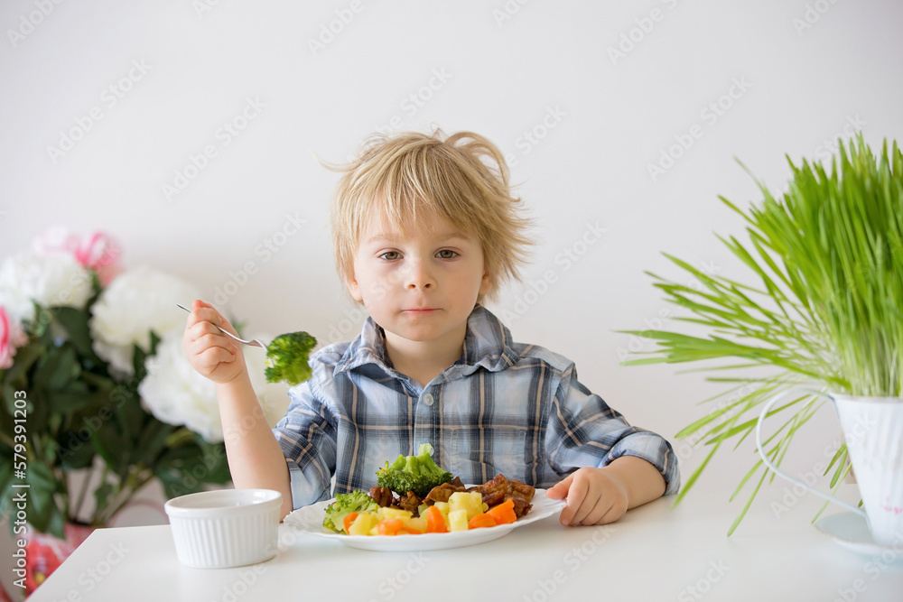 Little toddler child, blond boy, eating boiled vegetables, broccoli, potatoes and carrots with fried chicken meat at home Little toddler child, blond boy, eating boiled vegetables, broccoli, potatoes and carrots with fried chicken meat at home