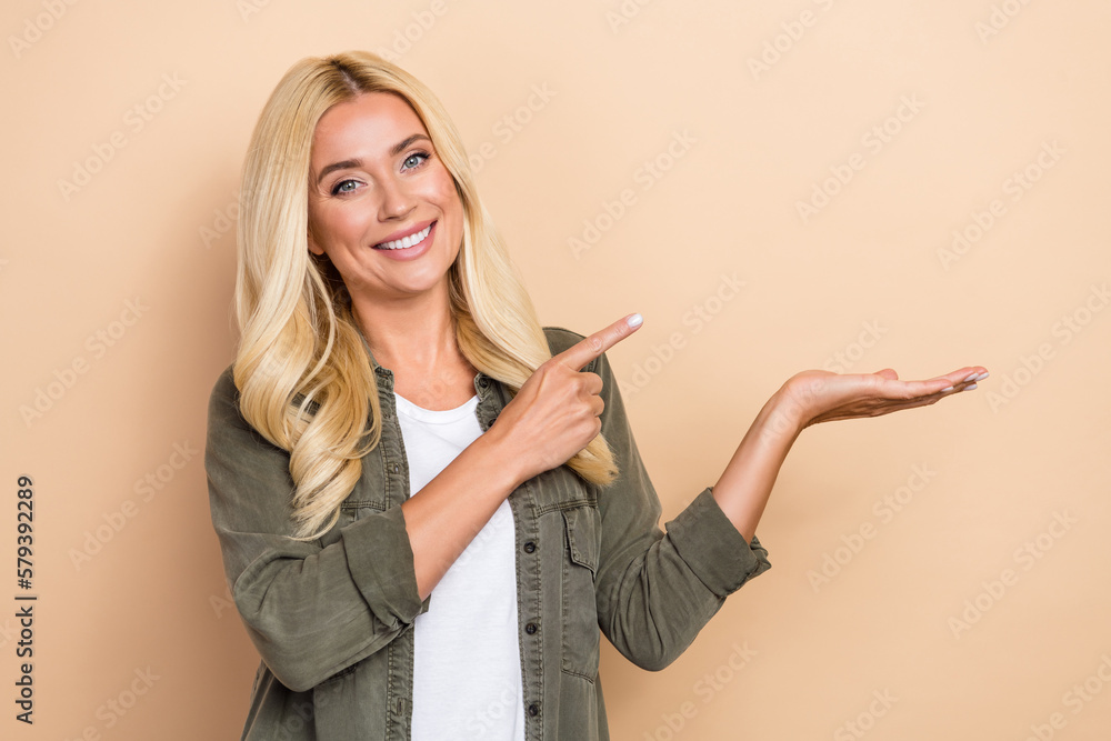 Photo of adorable cute woman wear khaki shirt pointing holding arm empty space isolated beige color background Photo of adorable cute woman wear khaki shirt pointing holding arm empty space isolated beige color background