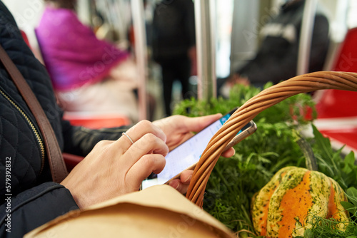 Woman returning from farmers market on a tram, looking at her phone photo