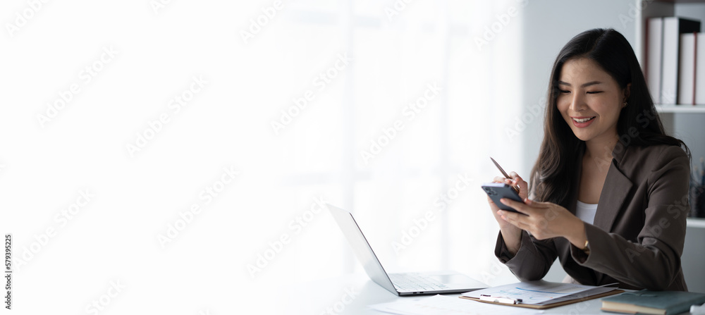 Young charming businesswoman using smartphone while working on laptop computer in office room. Young charming businesswoman using smartphone while working on laptop computer in office room.