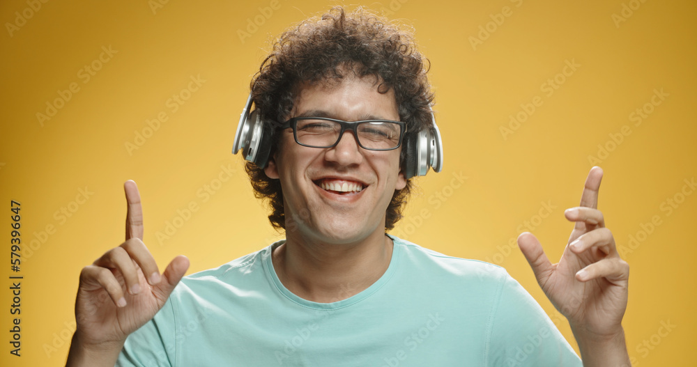 Close up shot of happy asian guy with curly hair putting on headphones and dancing, isolated on yellow background - leisure, fun concept Close up shot of happy asian guy with curly hair putting on headphones and dancing, isolated on yellow background - leisure, fun concept
