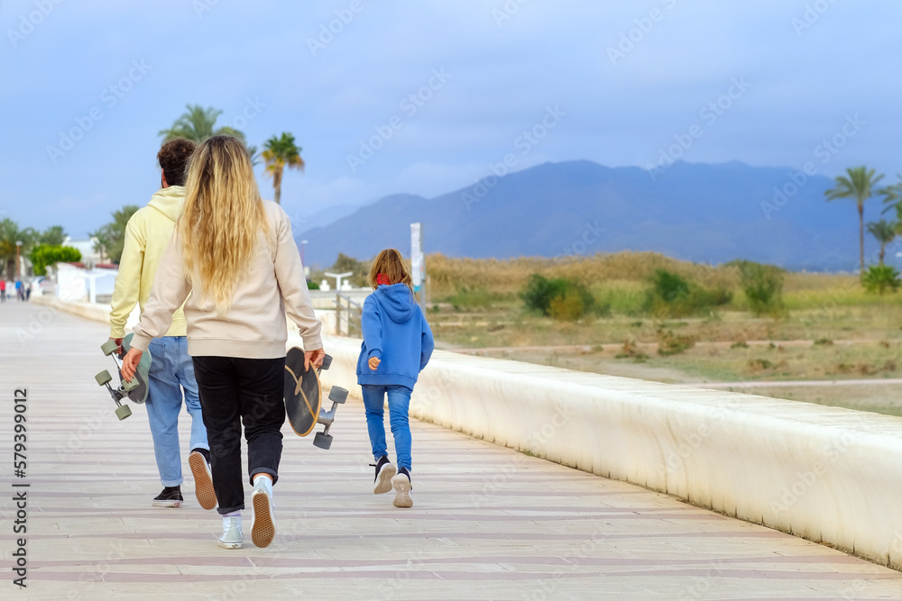 Happy family weekend. Mother father and doughter leisure and outdoor activity. riding on skateboards. Father holding and training his little child to ride a skateboard. Parenting. copy space