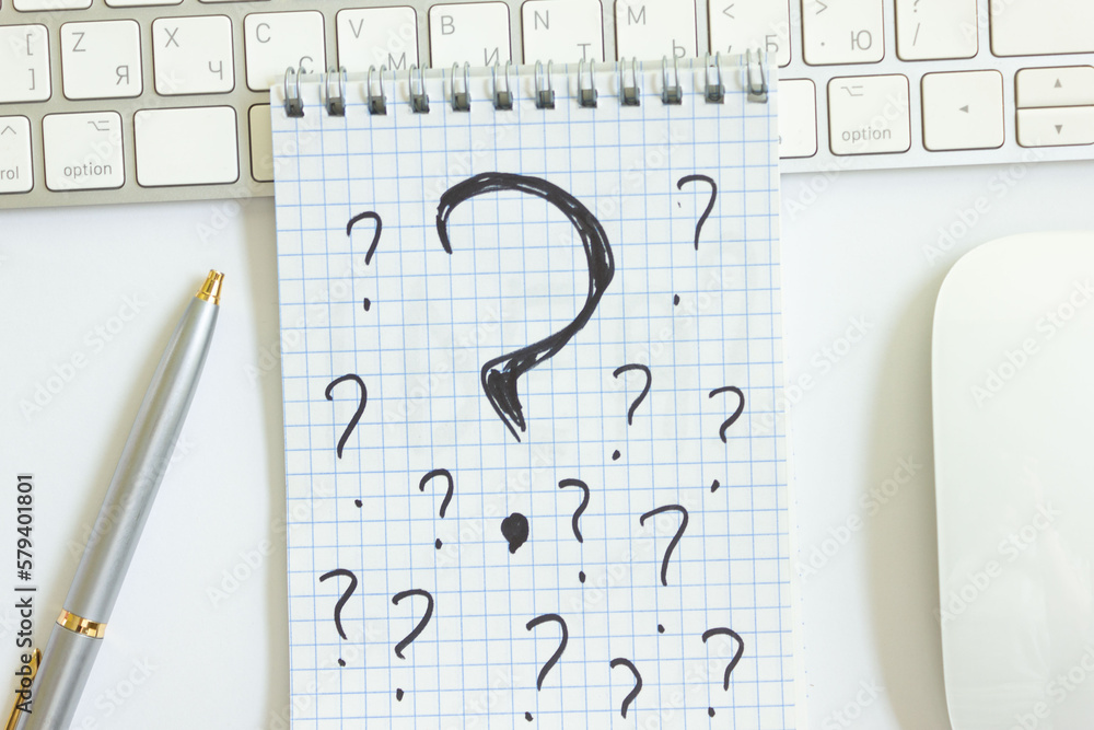 Question marks in a notepad on a desk with a keyboard from a computer