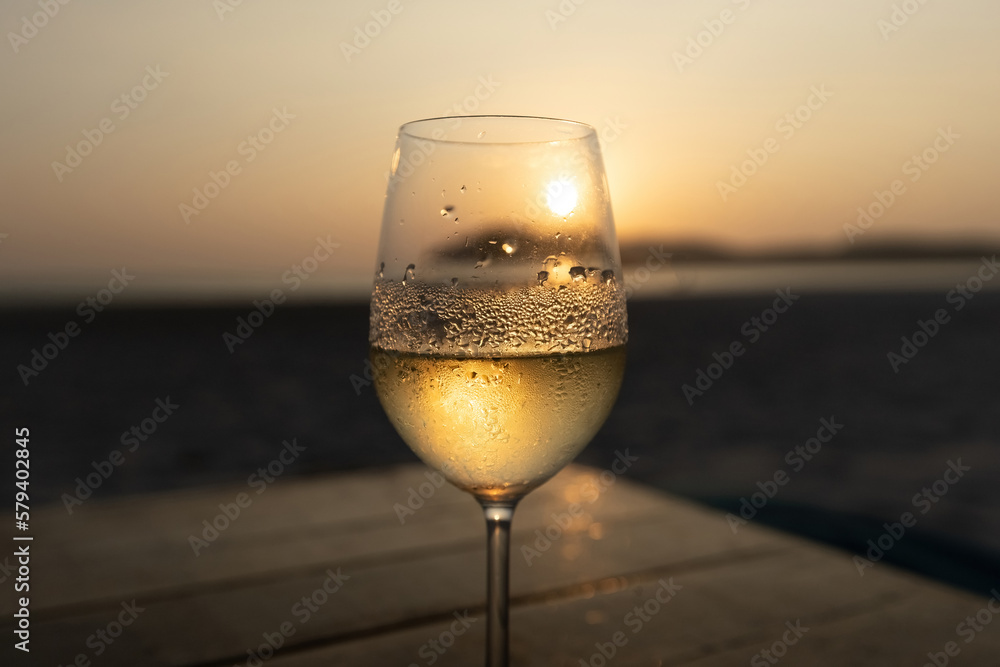 White wine in the misted glass against the sunset sky on the beach