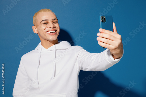 Fotografia Young dyed blond man of African American ethnicity wear white hoody do selfie shot on mobile cell phone post photo on social network isolated on plain dark royal navy blue background studio portrait