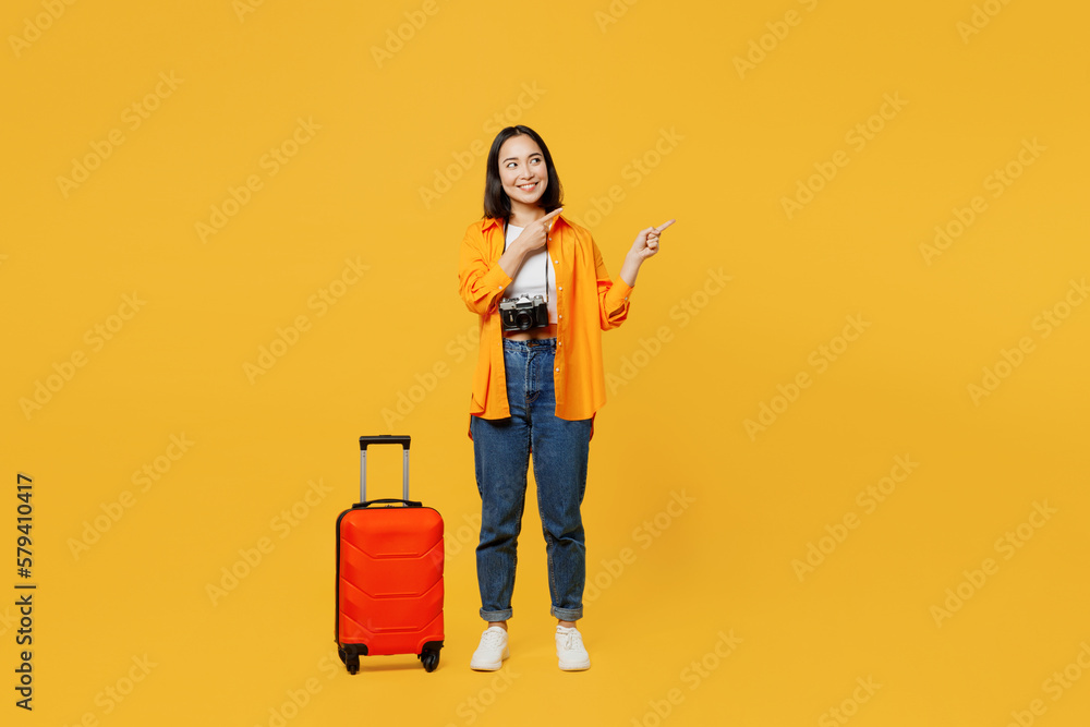 Young woman in summer casual clothes stand near suitcase point finger aside isolated on plain yellow background. Tourist travel abroad in free spare time rest getaway Air flight trip journey concept Young woman in summer casual clothes stand near suitcase point finger aside isolated on plain yellow background. Tourist travel abroad in free spare time rest getaway Air flight trip journey concept