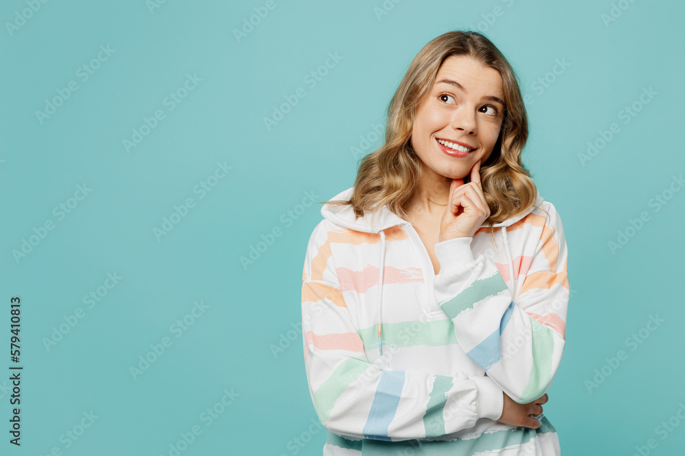 Young minded fun caucasian blonde woman wearing hoody put hand prop up on chin, lost in thought and conjectures isolated on plain pastel light blue cyan background studio portrait. Lifestyle concept. Young minded fun caucasian blonde woman wearing hoody put hand prop up on chin, lost in thought and conjectures isolated on plain pastel light blue cyan background studio portrait. Lifestyle concept.