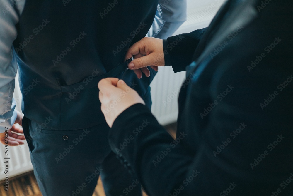 Male hands helping groom to wear costume