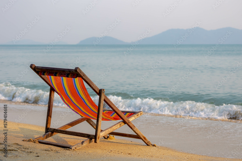 Vacation concept, Colourful canvas stretcher or beach chairs on the white sand beach with blurred view as background, Relaxing on seaside with sea wave approaching on the seashore in tropical islands.