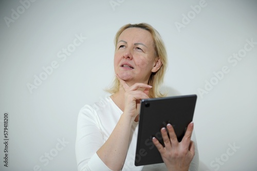 adult woman with tablet in hands thoughtfully supports chin with finger looks up to order