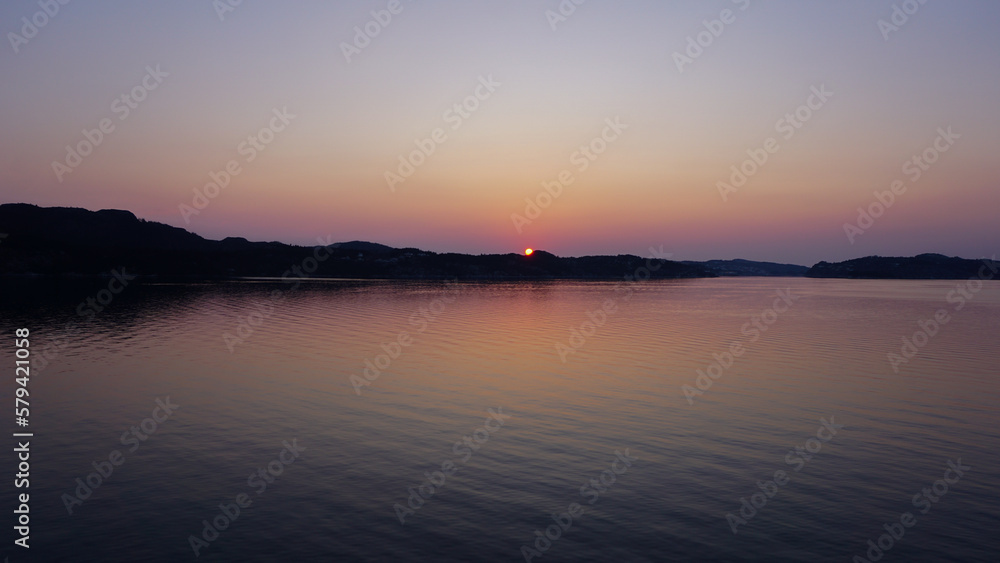 Colorful sunset over a lake, bits of land and mountains in the background