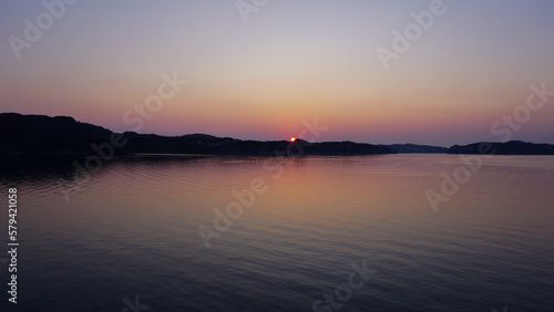 Colorful sunset over a lake, bits of land and mountains in the background