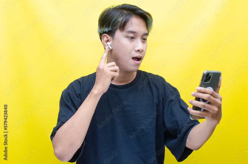 An enthusiastic Asian man with peek-a-boo hair is using airpods while dancing joyfully, checking his phone, and listening to music. An enthusiastic Asian man with peek-a-boo hair is using airpods while dancing joyfully, checking his phone, and listening to music.