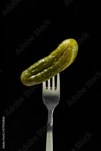 Pickled cucumber on a fork on a black background