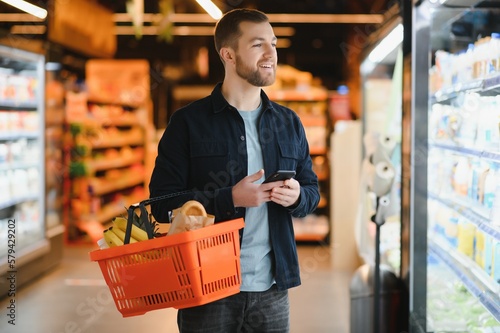 Handsome man buying some healthy food and drink in modern supermarket or grocery store Fototapet