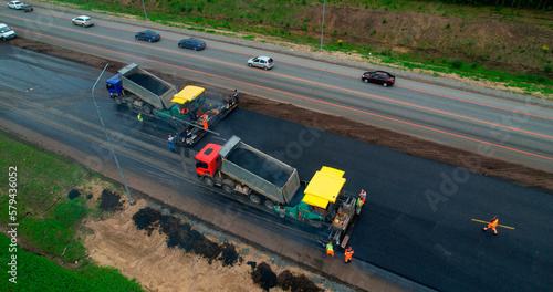 Road construction works aerial view. Laying of new asphalt on the road. The paver lays fresh asphalt, road rollers level and compact asphalt. 