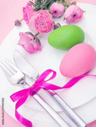 Happy Easter celebration table. Easter eggs and flower decoration on plates, pink background.