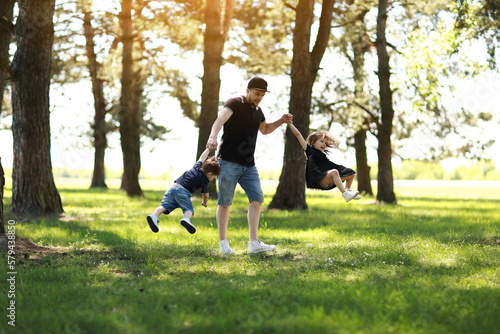 Fathers day. Happy dad having fun and spins two kids outdoors. Single daddy with little son and daughter relaxing in summer park. Family day and childhood concept. Active funny games, lively play