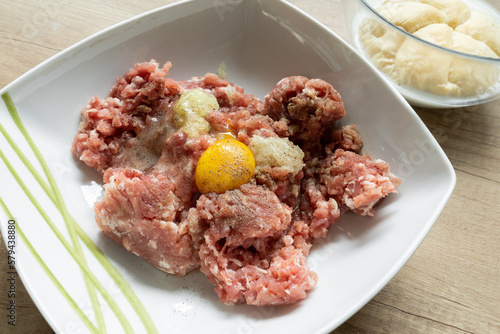 Minced meat, egg, onion and spices in a bowl. Preparing minced cutlets in Poland, traditional Polish kotlety mielone. Roll dipped in milk in background.