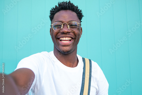 Selfie of cheerful handsome man in the street. Portarit of happy young man doing a selfie photo on the camera on a turquoise background wall.