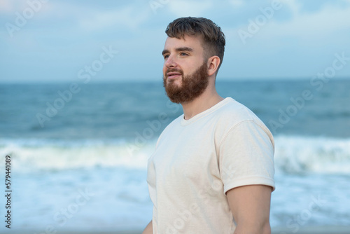 Portrait of happy young bearded guy, handsome man on the sea or ocean walking on beach enjoying good summer weather at vacation in tropical country