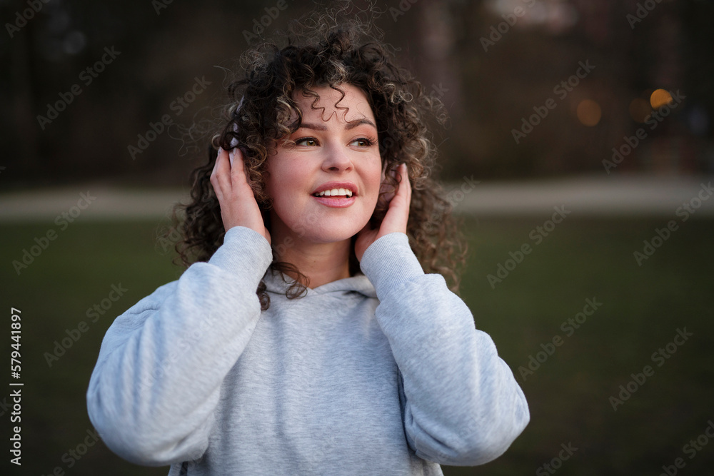Young beautiful woman in a gray sports hoodie, wearing headphones, listening to music in the evening in the park Young beautiful woman in a gray sports hoodie, wearing headphones, listening to music in the evening in the park
