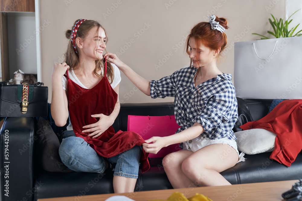 Obraz premium Staged photo. Lesbian couple at home. Young girls having a good time together. One of them went shopping. She bought a gorgeous burgundy velvet dress. Velvet suits you, honey!