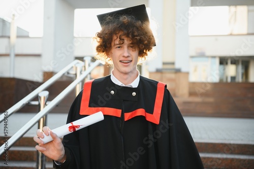 excited graduate student in gown with risen hands holding diploma.