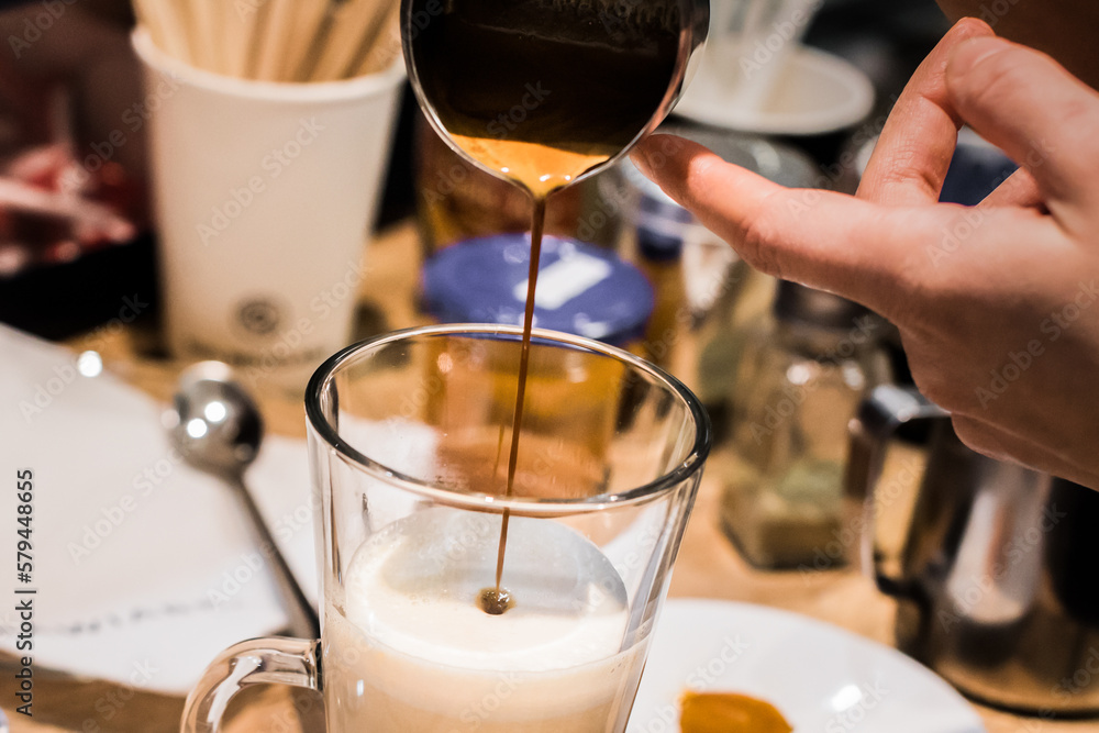 barista pouring shot of espresso into the glass with foamed milk making latte, closeup barista pouring shot of espresso into the glass with foamed milk making latte, closeup