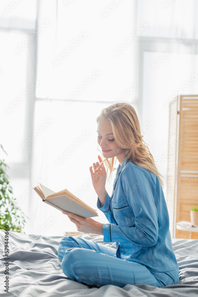 satisfied young woman in blue silk nightwear reading book while resting on weekend. satisfied young woman in blue silk nightwear reading book while resting on weekend.