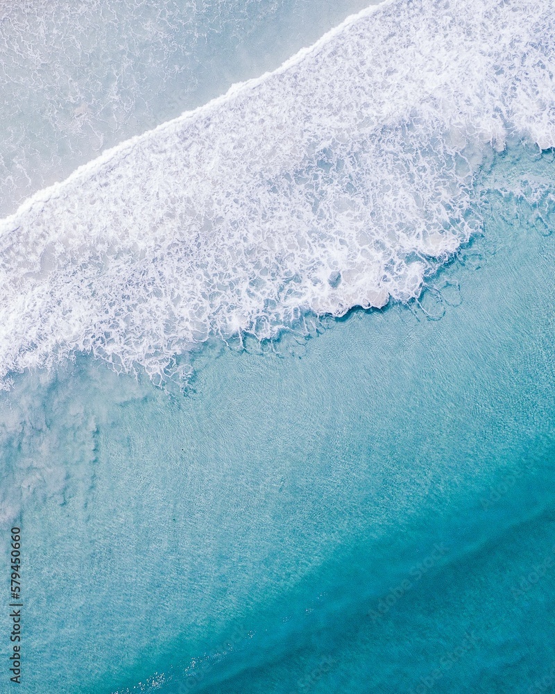 Fototapeta premium Vertical aerial shot of clear ocean water with foamy waves in Western Australia