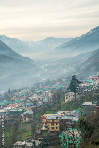 View in town Kullu. Woman standing on balcoon in sunbeams and looking at cow ( Holy animal in India)