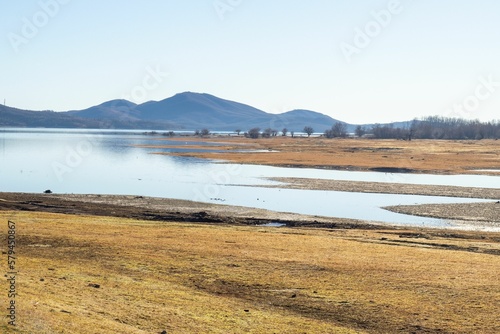 Scenic shot of the coast of a lake surrounded by hills under the blue sky