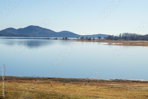 Scenic shot of the coast of a lake surrounded by hills under the blue sky