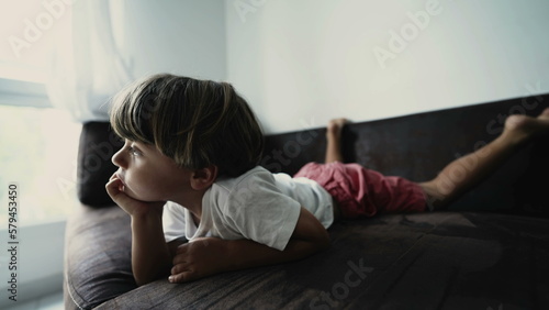 One small boy lying on couch watching cartoons off camera. A relaxed kid laid on sofa