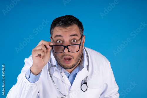 young doctor man with surprise expression on blue isolated background. medical checkup concept.
