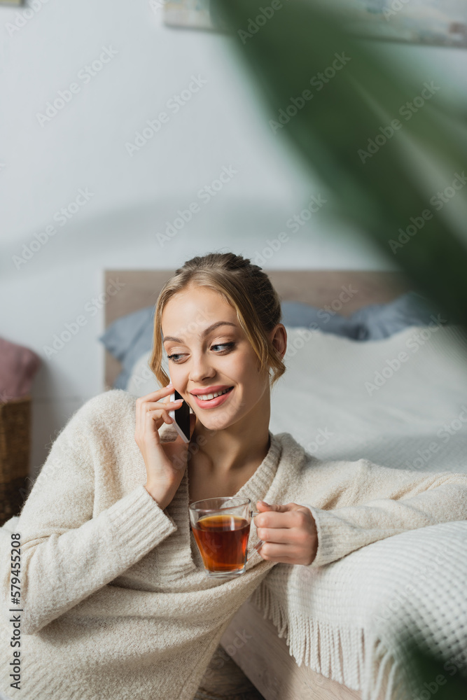 satisfied woman talking on smartphone and holding glass cup of tea in bedroom. satisfied woman talking on smartphone and holding glass cup of tea in bedroom.
