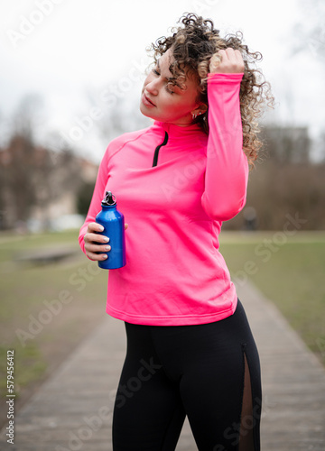 Young active sportywoman in a bright suit holds a bottle of water, for sports