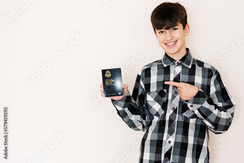 Young teenager boy holding Costa Rica passport looking positive and happy standing and smiling with a confident smile against white background. photo