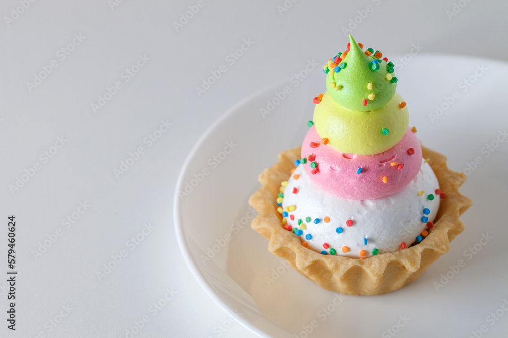 Cake basket tart with three-layer multicolored custard sweet sprinkles on white board background, selective focus