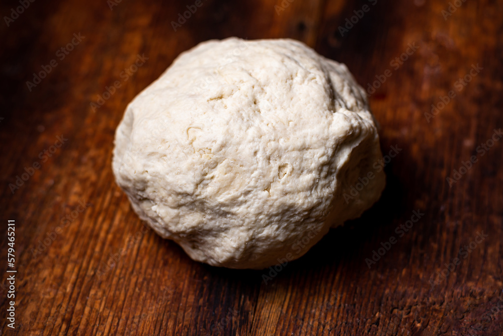 Fototapeta premium Ball of dough on wooden surface. Preparation of shiver dough for making bread, base for pizza, baguettes.