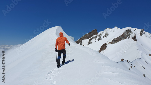 A male climber with a hiking pole walks to the top of the snow-capped mountain. Erciyes Mountain east ridge route in Kayseri, Turkey