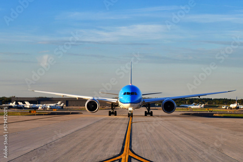 A jumbo jet airplane taxing on the runway preparing to take off with the airport in the background