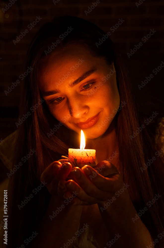A woman holds a burning candle in her palms on a dark black background A woman holds a burning candle in her palms on a dark black background
